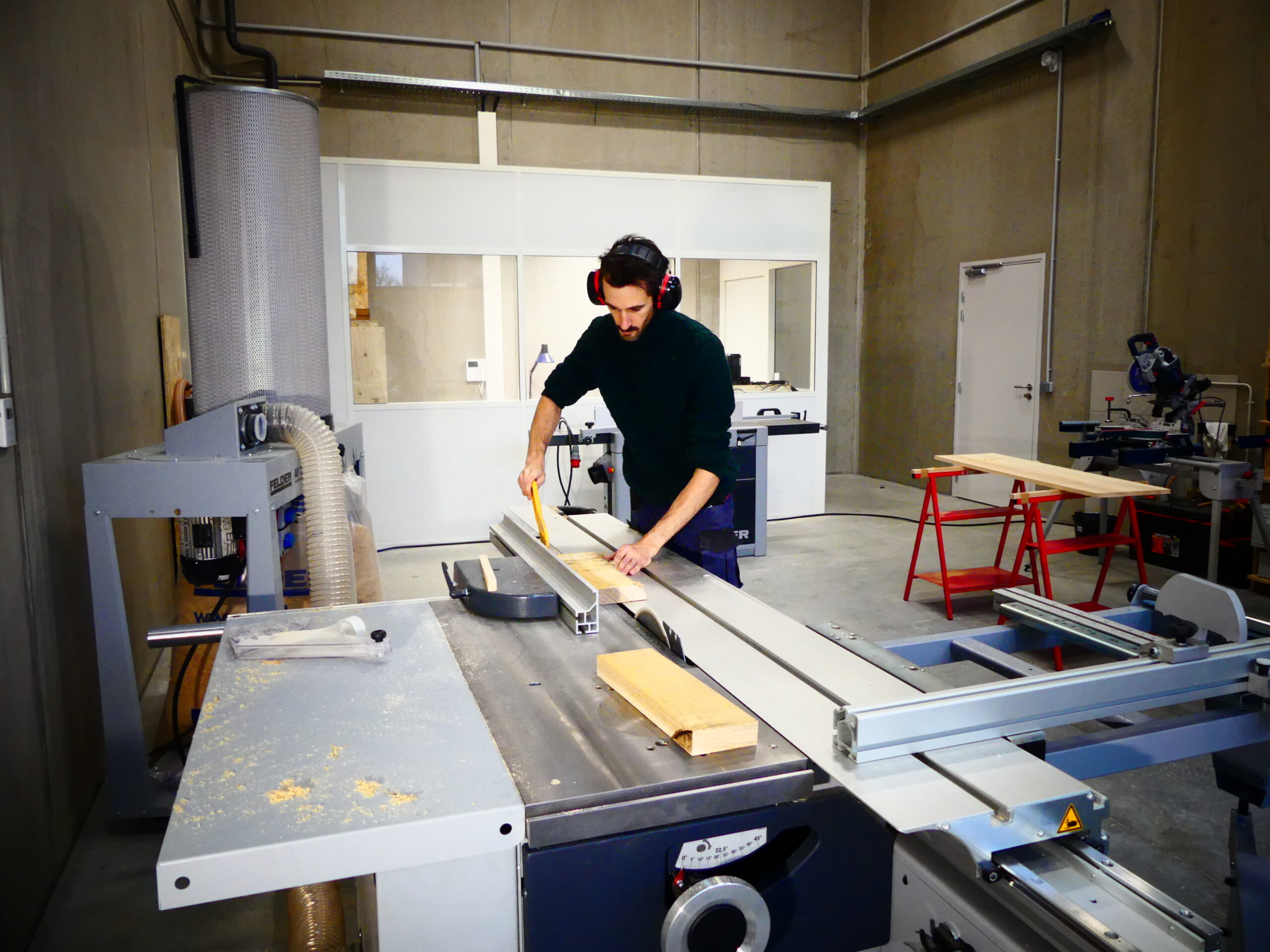 Ébéniste utilisant une scie à panneaux pour découper une planche de bois massif dans l'atelier Paul de Bazelaire